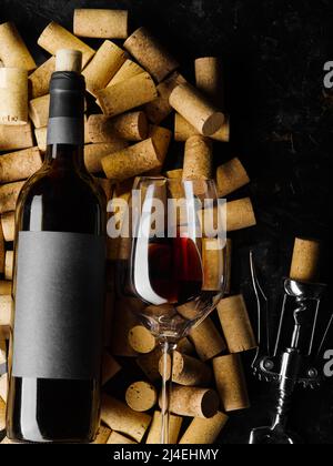 Auf schwarzem Hintergrund gibt es viele Weinkorken, eine Flasche Rotwein, einen Korkenzieher und ein Weinglas mit Wein. Feiertag, Geburtstag, Jahrestag, Verbot Stockfoto