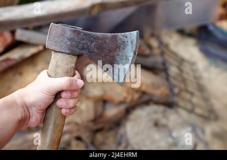 Mann mit Axt. Axt in der Hand. Ein starker Mann hält eine Axt in den Händen vor dem Hintergrund von Feuerholz. Selektiver Fokus, unscharfer Hintergrund Stockfoto