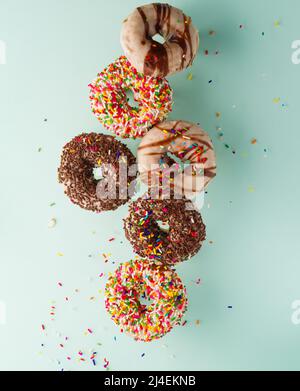 Mehrfarbige Donuts, die bei einem gefrorenen Flug auf hellblauem Hintergrund mit Schokolade- und Zuckereisung überzogen sind. Süßes Essen, Geburtstag, Urlaub, Glück ho Stockfoto