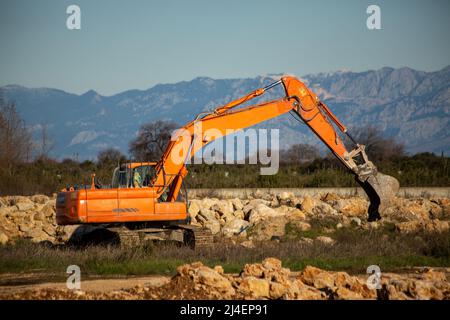 Raupenbagger, der Steinhaufen freiräumt. Orangefarbenes Gerät Stockfoto