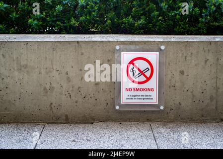 Rot-weißes Rauchverbotsschild an der Wand draußen in der Nähe des Fußgängerwegs. Stockfoto