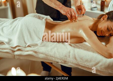 Professionelle männliche Therapeutin, die mit den speziellen Tassen eine Vakuummassage macht. Chinesische Massage Stockfoto