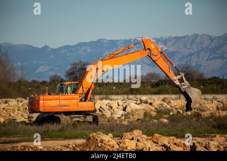 Raupenbagger, der Steinhaufen freiräumt. Orangefarbenes Gerät Stockfoto