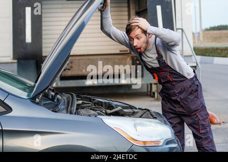 Schockierter Mechaniker schaut in das Auto. Motorstörung. Stockfoto