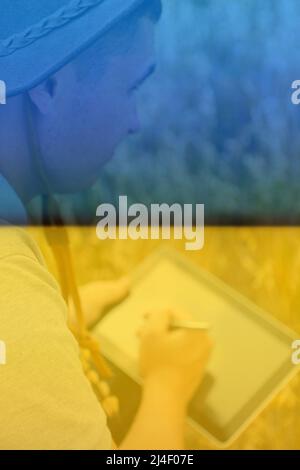 Ukrainische Farm. Porträt eines Bauern, der im goldenen Weizenfeld sitzt und auf dem Tablet scrollt. Junger Mann mit Cowboyhut auf dem Feld, der Weizenernte untersucht. Au Stockfoto