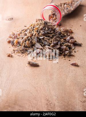 maldivische Fischchips, verstreut auf einer Holzoberfläche aus dem Behälter, getrocknete und ausgehärtete Fischstücke, starkes Aroma und aromatische Zutat Stockfoto