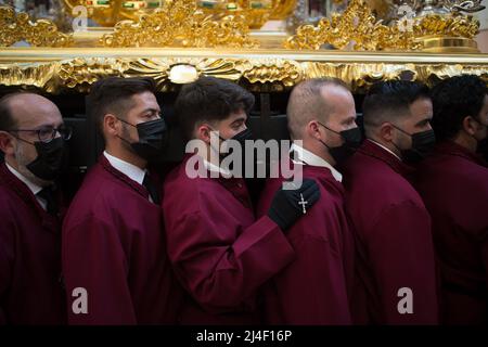 Ein Büßer der Bruderschaft „Vineros“ wird während des Gründonnerstags, anlässlich der Feierlichkeiten der Karwoche, ein Kreuz halten und einen verzierten Wagen mit der Statue Christi tragen sehen. Nach zwei Jahren ohne Karwoche aufgrund der Coronavirus-Pandemie warten Tausende von Gläubigen darauf, die Prozessionen mit den Statuen von Christus und der Jungfrau Maria im Rahmen der traditionellen Karwoche auf den Straßen zu sehen. In Andalusien versammelt die Karwoche Tausende von Menschen aus allen Ländern und gilt als eines der wichtigsten religiösen und kulturellen Ereignisse des Jahres. Stockfoto