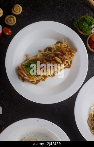 Eine gekochte Pasta-Spaghetti mit schwarzer Pfeffersauce, Rindfleisch, Olivenöl und frischer grüner Petersilie in einem weißen ovalen Teller mit Zutaten Stockfoto