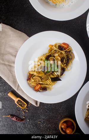Eine gekochte Pasta-Spaghetti mit Pilzsauce, Rindfleisch, Olivenöl und frischer grüner Petersilie in einem weißen ovalen Teller mit Zutaten auf schwarzem Hintergrund Stockfoto