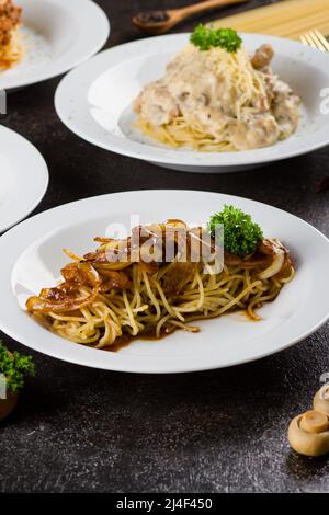 Eine gekochte Pasta-Spaghetti mit schwarzer Pfeffersauce, Rindfleisch, Olivenöl und frischer grüner Petersilie in einem weißen ovalen Teller mit Zutaten Stockfoto