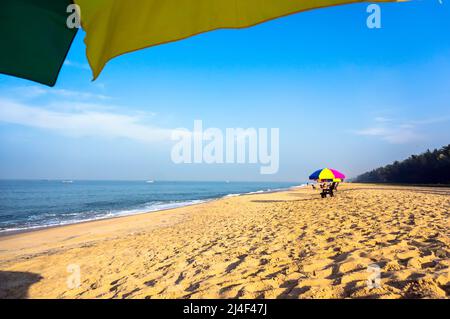 Entspannen Sie sich am Strand unter Sonnenschirmen im Schatten. Strandliegen am weißen Sandstrand mit wolkenblauem Himmel und Sonne. Mararikulam Kerala Indien Stockfoto