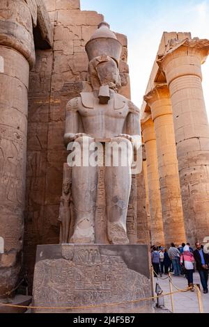 Luxor, Ägypten - 2. Januar 2012 : Statue des Pharao Ramses II. Mit der großen Kolonnade und unbekannten Touristen zu Fuß im Luxor Tempel, Luxor, Ägypten. Stockfoto