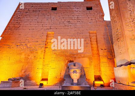 Nachtszene des Kopfes der großen Statue des Pharao Ramses II vor dem Mast des Luxor-Tempelkomplexes in Luxor, Ägypten. Stockfoto