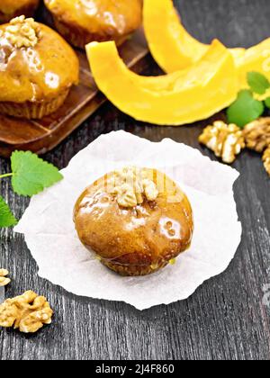 Kleiner Kürbis-Cupcake mit orangefarbener Glasur und Walnüssen auf Papier, Minze-Zweige auf dunklem Holzbrett-Hintergrund Stockfoto