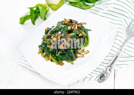 Spinat gebraten mit Zwiebeln in einem Teller auf einem Handtuch vor dem Hintergrund von Holzbrett Stockfoto