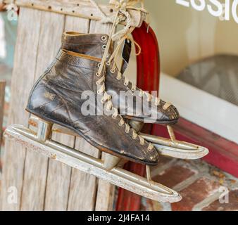 Vintage Paar Herren Schlittschuhe, die an einer Holzwand hängen. Straßenfoto, Niemand, selektiver Fokus Stockfoto