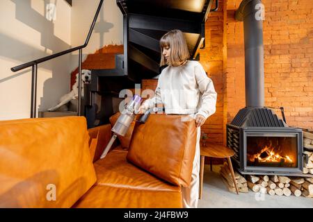 Frau saugt Couch mit kabellosem Handstaubsauger Stockfoto