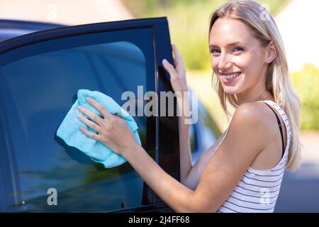 Junge Frau, die ihr Auto im Freien putzt Stockfoto