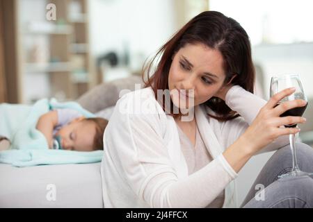 Frau mit einem Glas Rot und schlafenden Babys Stockfoto