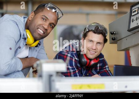 Portrait von zwei Mechanikern, die moderne Laserschneidemaschine reparieren Stockfoto
