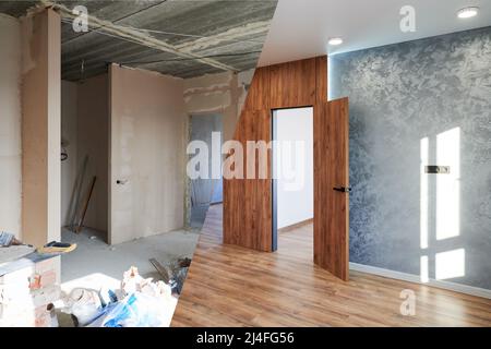 Leere Wohnung mit Eingang vor und nach der Restaurierung. Vergleich von altem Zimmer mit Baumaterialien und neuem Zimmer mit Holztür, Parkettboden und grauer Wand. Konzept der Renovierung. Stockfoto