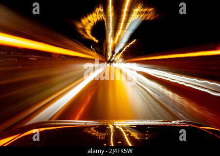 Bewegungsunschärfe von Straßenlaternen aus einem fahrenden Auto, die den Eindruck von Geschwindigkeit vermitteln Stockfoto