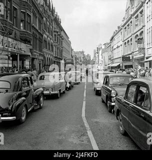 Ein sehr geschäftiges Stadtbild in Oxford – ein Blick nach Norden auf die Cornmarket Street, Oxford, Oxfordshire, England, Großbritannien von der Kreuzung mit der High Street im Jahr 1960. Zu dieser Zeit war die Straße sehr autoorientiert und es scheint ein Stau mit Autos zu sein, die stillstehen. Ein Polizist befindet sich in der Mitte der Straße. Auch Käufer sind in Hülle und Fülle vorhanden. Heute wurde die Straße weitgehend zur Fußgängerzone erklärt – ein altes Foto aus dem Jahr 1960s. Stockfoto