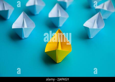 Führungskonzept - Gelb Farbe Papier Schiff Origami führt den Rest des weißen Papierschiffs auf blauem Cover Hintergrund. Speicherplatz kopieren Stockfoto