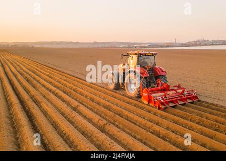 PRAG , TSCHECHISCHE REPUBLIK - MÄRZ 18 2022: Schwerer Traktor verwendet Pflug, um Betten für die Pflanzung von Kartoffeln in landwirtschaftlichen Feldern zu machen. Die leistungsstarke Maschine arbeitet auf dem Bauernhof bei sonniger Tagesansicht Stockfoto