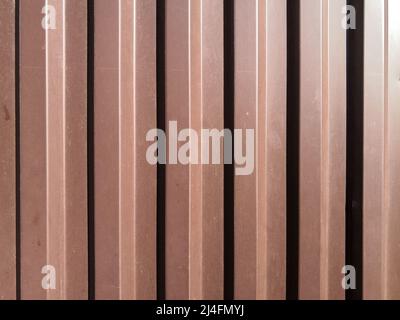 Blick auf ein gewelltes braunes Eisenblech mit senkrechten Wellen, die bei hellem Sonnenlicht von der Seite beleuchtet werden. Der Kontrast von Licht und Schatten. Stockfoto