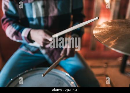 High Angle of Crop anonymer Schlagzeuger mit Drumsticks, die während der Probe im Studio Schlagzeug spielen Stockfoto
