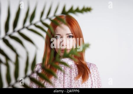 Frau mit mittlerem Erwachsenenalter versteckt sich hinter den Palmblättern der Hauspflanze Stockfoto