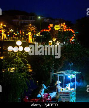 Nacht in der Altstadt von Hoi an mit einem Straßenverkäufer und einer Brücke in der Ferne, aber auf dem oberen Bildrand. Stockfoto