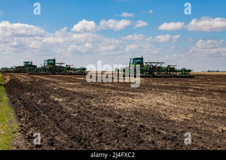 Provinz Nordkasachstan, Kasachstan - 12. Mai 2012: Frühjahrsaat. John Deere-Traktoren, die den Boden mit Egge kultivieren. Blauer Himmel, Wolken Stockfoto