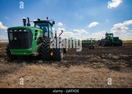 Provinz Nordkasachstan, Kasachstan - 12. Mai 2012: John Deere-Traktoren, die in der Aussaat Boden mit Pflügen anbauen. Blauer Himmel, Wolken Stockfoto