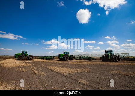 Provinz Nordkasachstan, Kasachstan - 12. Mai 2012: John Deere-Traktoren kultivieren Boden mit Pflügen. Frühjahrsaat-Kampagne. Blauer Himmel, Wolken. panor Stockfoto