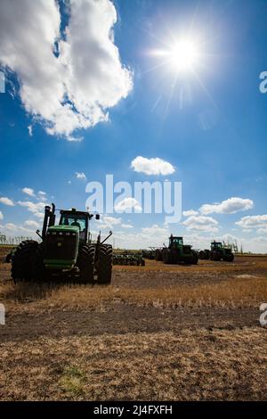 Provinz Nordkasachstan, Kasachstan - 12. Mai 2012: Frühjahrsaat. John Deere-Traktoren, die mit Pflügen Boden kultivieren. Blauer Himmel, Wolken Stockfoto