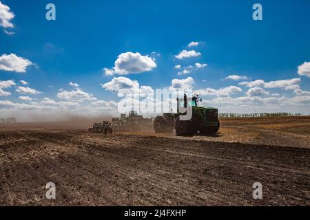 Provinz Nordkasachstan, Kasachstan - 12. Mai 2012: Aussaat-Kampagne. John Deere-Traktoren, die den Boden mit Egge kultivieren. Blauer Himmel, Wolken Stockfoto