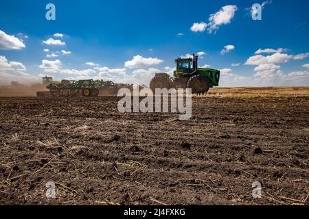 Provinz Nordkasachstan, Kasachstan - 12. Mai 2012: Frühjahrsaat. John Deere Traktoren kultivieren Erde mit Egge.Blauer Himmel, Wolken Stockfoto