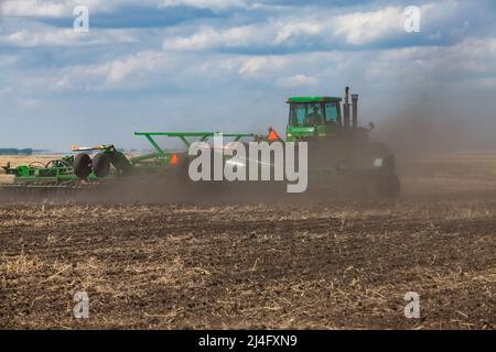 Provinz Nordkasachstan, Kasachstan - 12. Mai 2012: Aussaat-Kampagne. John Deere Traktor kultiviert Boden mit Pflug. Staubwolke. Blauer Himmel mit Wolken Stockfoto