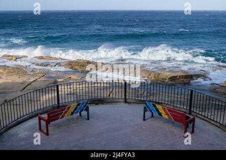 Bänke in traditionellen maltesischen Farben und Brandung brechen an einem windigen Wintertag in Sliema Malta Stockfoto