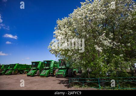 Provinz Nordkasachstan, Kasachstan - 12. Mai 2012: Frühjahrsaat. Landwirtschaftliche Maschinen (Mähdrescher) auf dem Parkplatz. Blühender Obstbaum rechts. Stockfoto