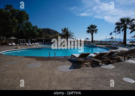 IOS, Griechenland - 12. Juni 2021 : Blick auf einen Außenpool mit Sonnenliegen und Palmen vor dem Mylopotas-Strand in iOS Griechenland Stockfoto