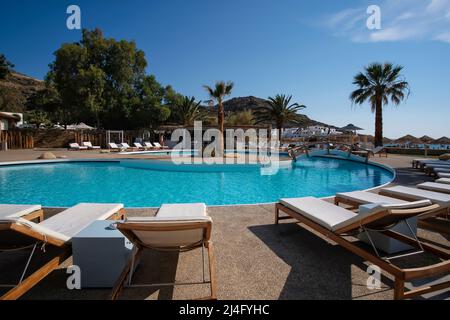 IOS, Griechenland - 12. Juni 2021 : Blick auf einen Außenpool mit Sonnenliegen und Palmen vor dem Mylopotas-Strand in iOS Griechenland Stockfoto