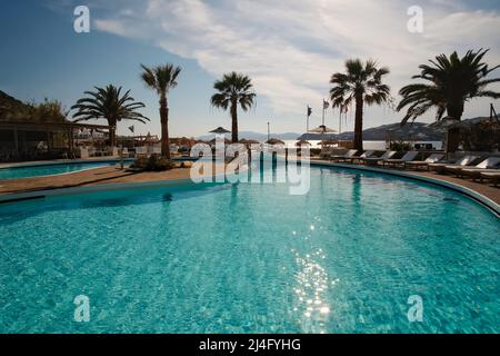 IOS, Griechenland - 12. Juni 2021 : Blick auf einen Außenpool mit Sonnenliegen und Palmen vor dem Mylopotas-Strand in iOS Griechenland Stockfoto