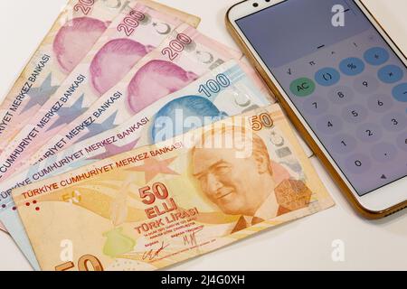 50, 100 und drei Stück 200 türkische Lira-Banknoten und Rechner-App öffnen Handy auf isoliertem Hintergrund. Zeit ist Geld Konzept. Stockfoto