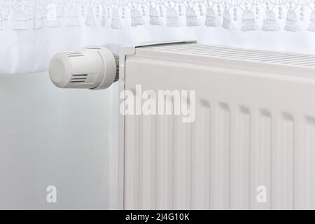 Weißer Heizkörper und Temperaturregler. Heizungsregler im selektiven Fokus. Stockfoto