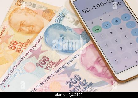 50, 100 und 200 türkische Banknoten und Taschenrechner-App öffnen Mobiltelefon auf isoliertem Hintergrund. Banknoten im selektiven Fokus. Zeit ist Geld Konzept. Stockfoto