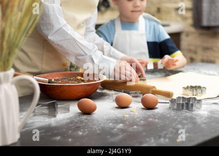 Mutter und Sohn schneiden auf einem schwarzen Holztisch, der zu Hause in der Küche mit Mehl bestreut ist, Formen zum Backen von süßen Plätzchen aus Blätterteig aus. Auswahl Stockfoto