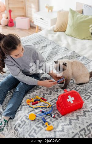 High-Angle-Ansicht des Mädchens, das mit einer Spielzeug-Spritze Injektion an die Katze macht Stockfoto